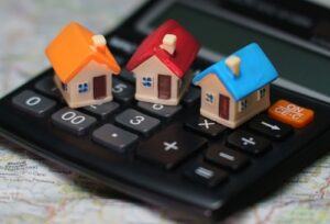  Three small model houses, each with different colored roofs (orange, red, and blue), on top of a calculator. How much should I charge for rent.
