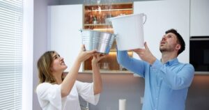 Man and woman holding buckets in the air as water leaks from a ceiling as they consider what makes an rental uninhabitable.