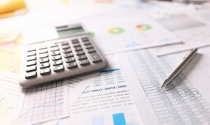 Close-up of a calculator, pen, and financial documents with charts and spreadsheets.