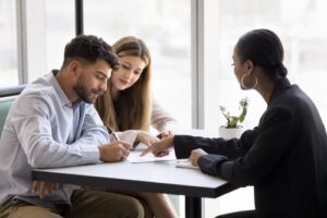 A couple signing documents at a table while a professional points to the paperwork.