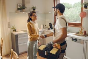 A woman shaking hands with a handyman in a modern kitchen after a service or repair job.